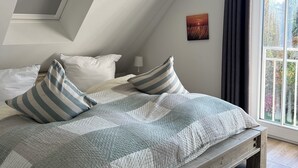A bedroom with a sloped ceiling, a bed with striped pillows, a quilted blanket, and a view of trees through a window. - Spacious vacation home near the beach in a quiet location in Rosenhagen (Dassow)