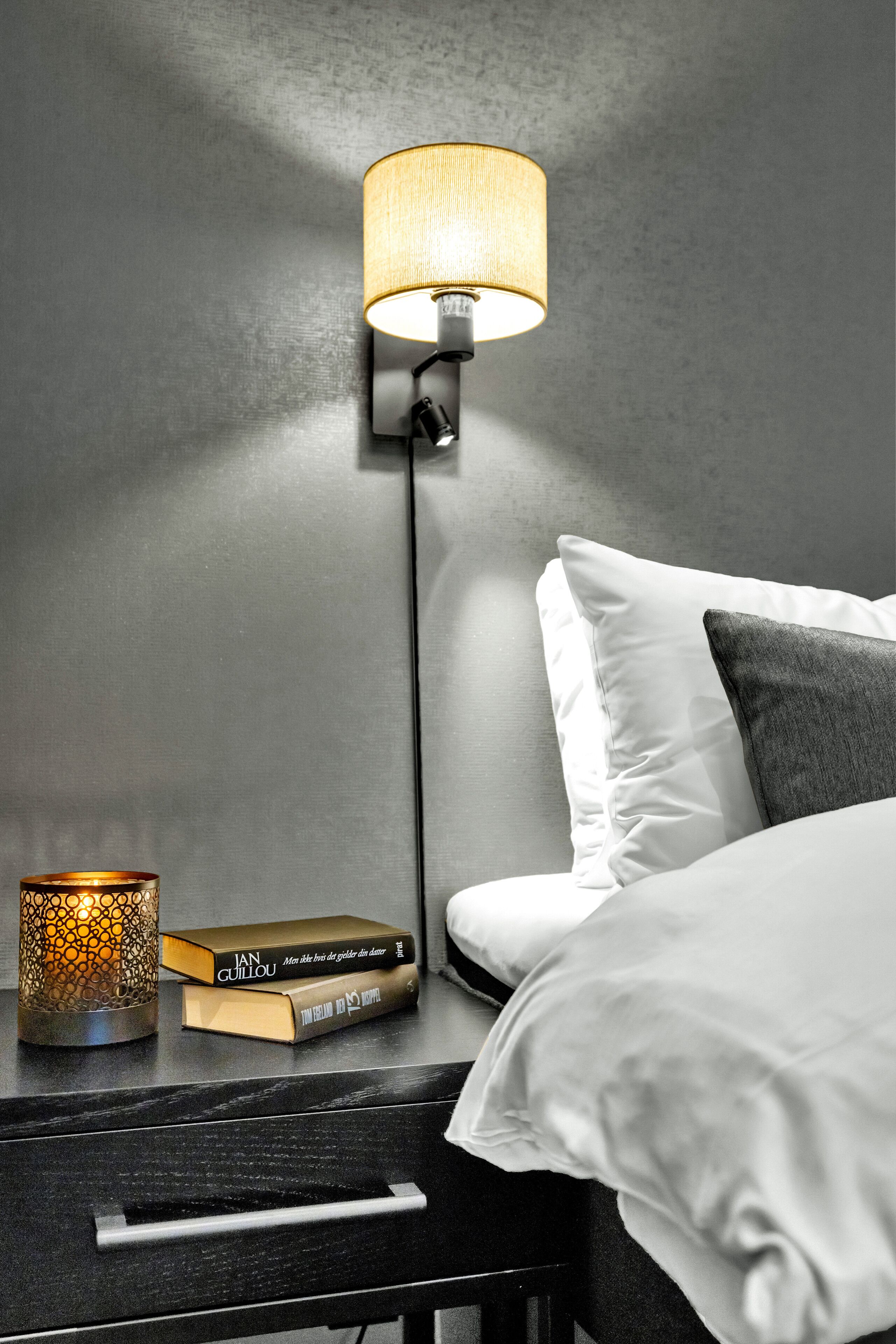 Un dormitorio moderno con una mesita de noche, una lámpara y libros.