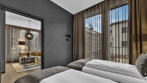 Habitación de hotel moderna con una cama grande, una mesita pequeña y vistas de la ciudad a través de amplios ventanales.