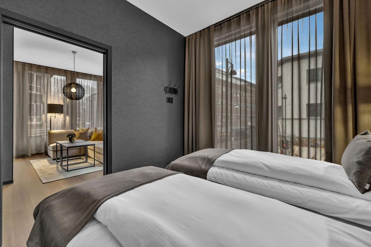 Una habitació d'hotel moderna amb un llit gran, una taula petita i vistes a la ciutat a través de grans finestres.