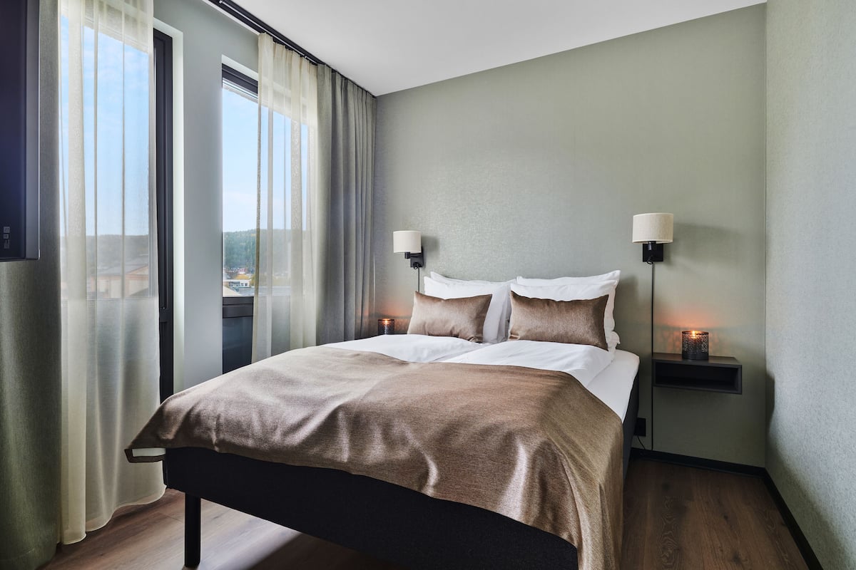 Una habitació d'hotel moderna amb un llit gran, dues làmpades de nit i vista per la finestra.