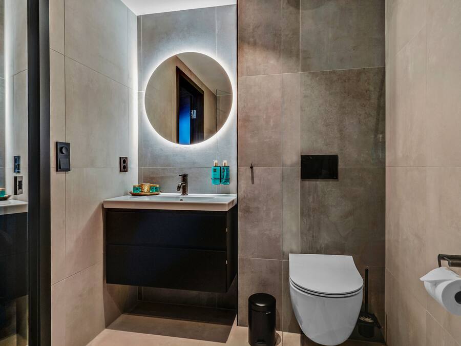 A modern bathroom with a round mirror, a sink, a toilet, and a trash bin.
