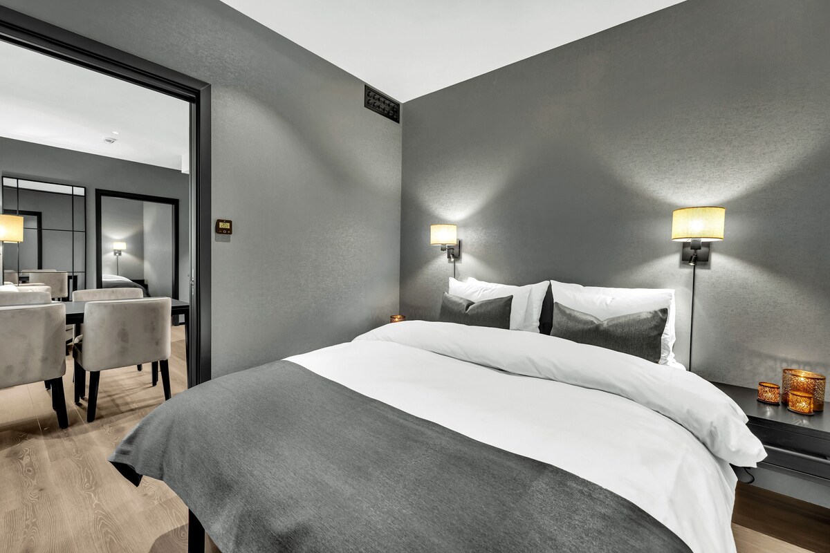 Une chambre d’hôtel moderne avec un grand lit, deux lampes de chevet, un miroir et une petite table avec des bougies.