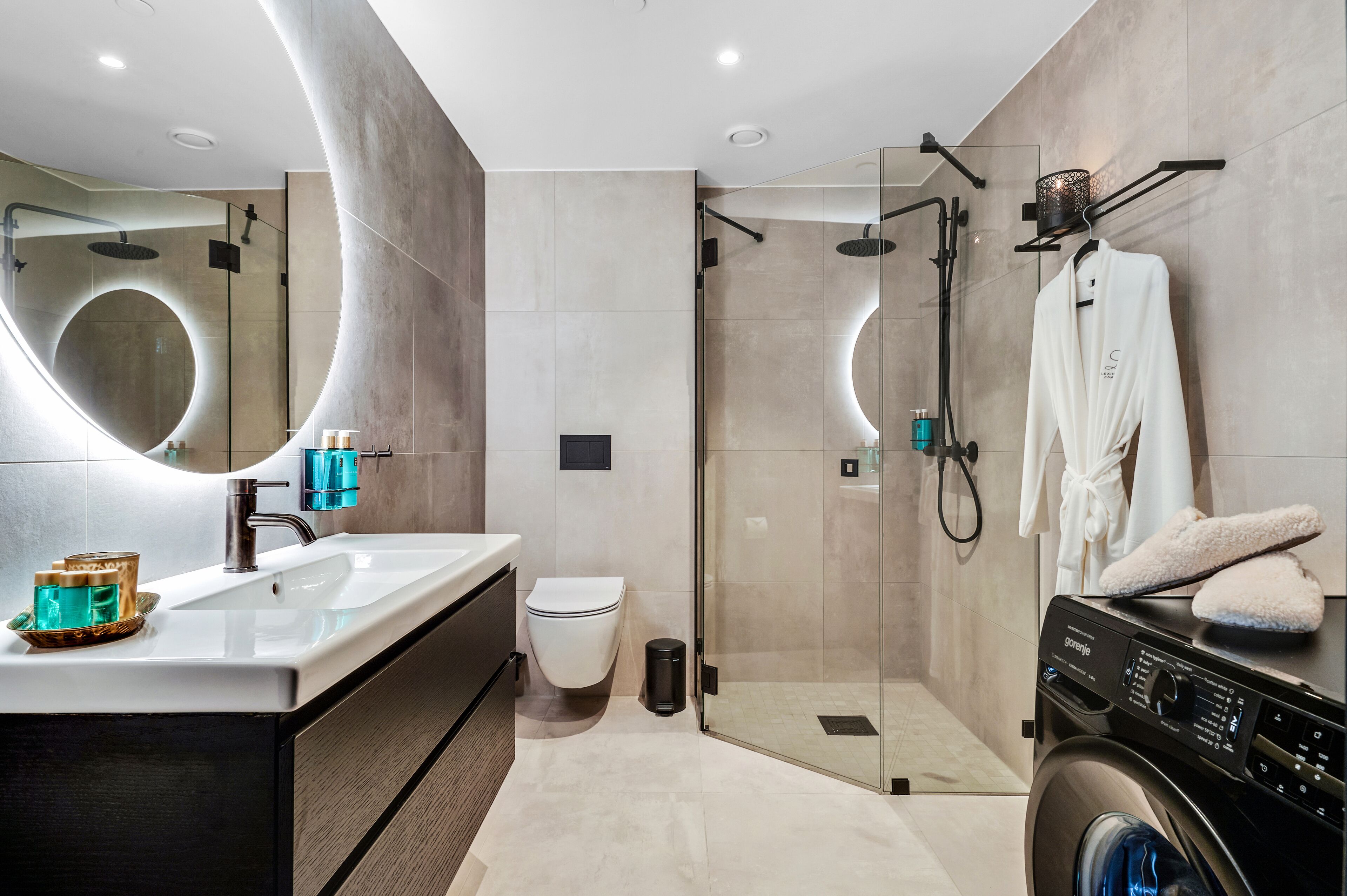 A modern bathroom with a glass-enclosed shower, a washing machine, and a large mirror.