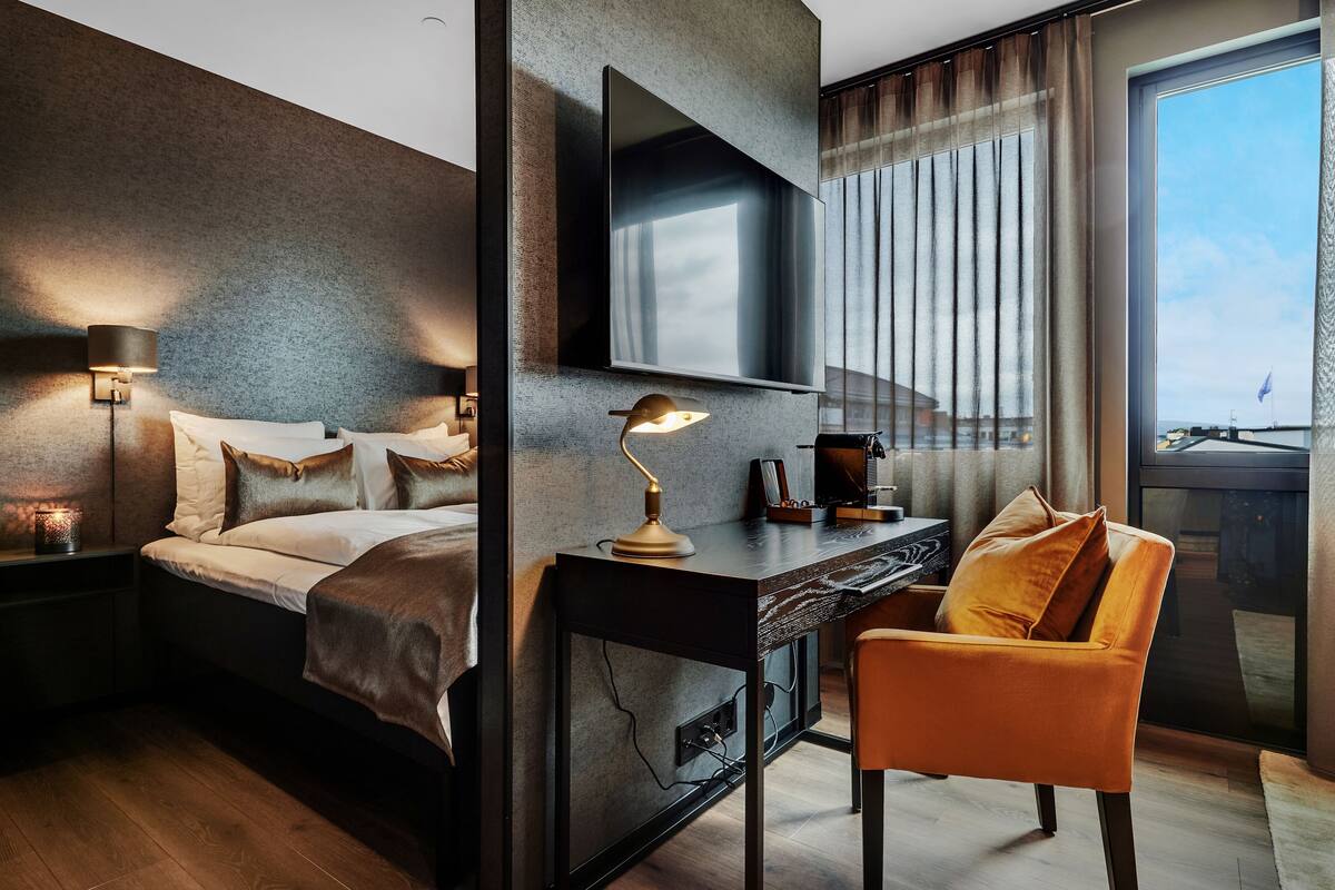 Habitació d'hotel moderna amb llit, escriptori, cadira i finestra gran.