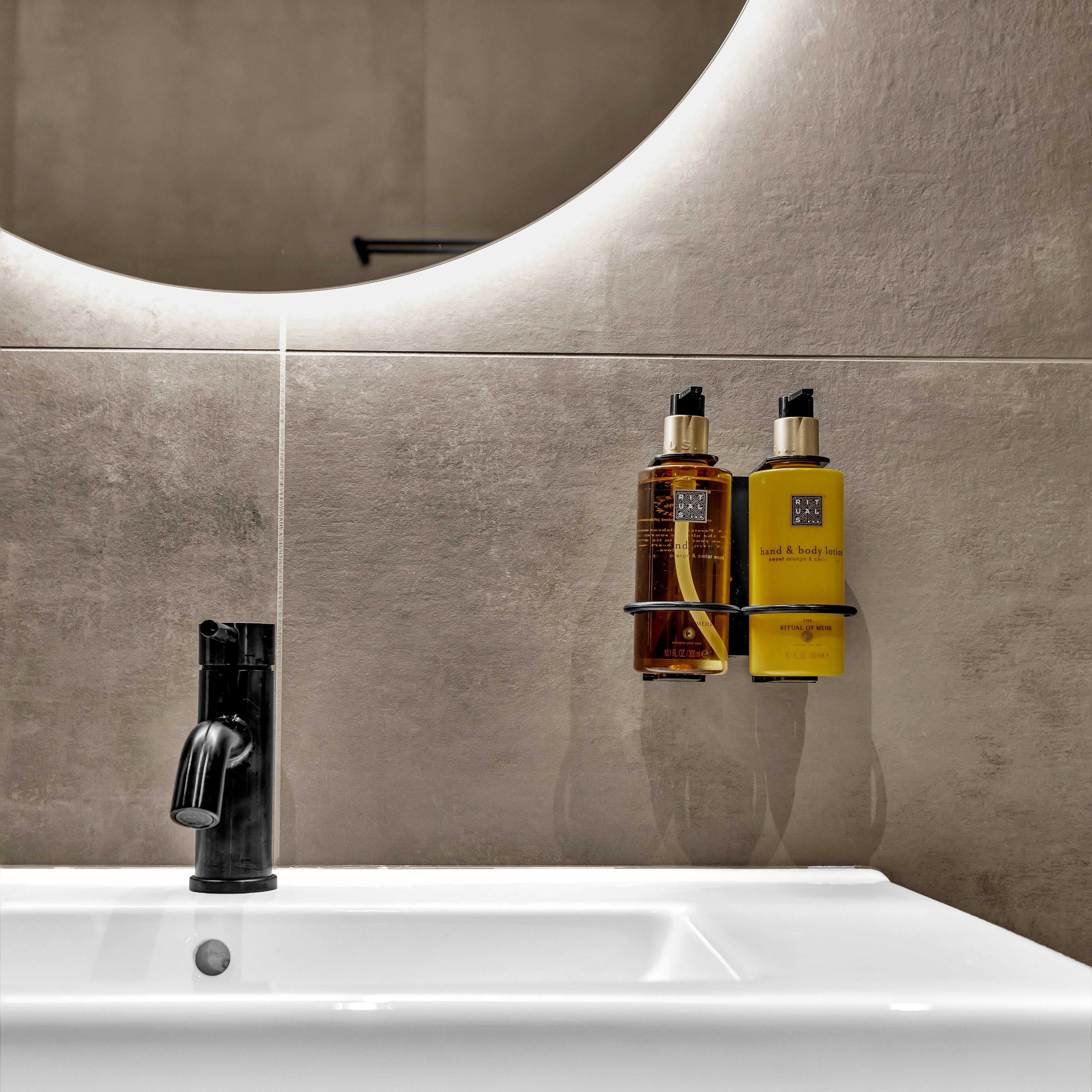 Un baño con un lavamanos blanco, dos botellas de crema para manos y cuerpo, y un grifo negro.
