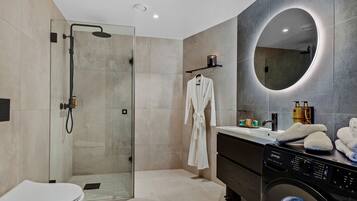 A modern bathroom with a glass-enclosed shower, a round mirror, a white robe, and a washing machine.
