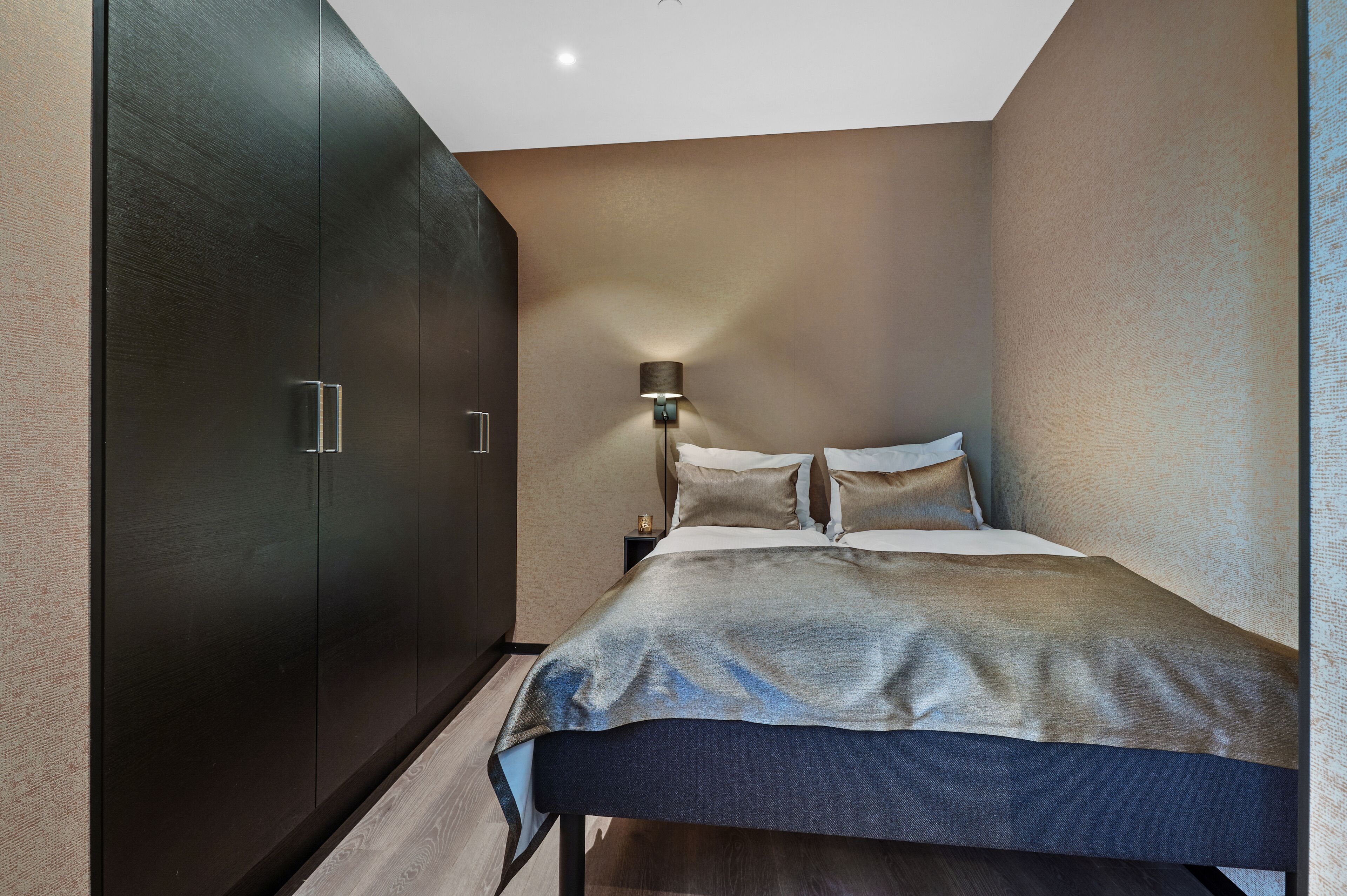 A bedroom with a bed, a nightstand, a lamp, and a wardrobe.