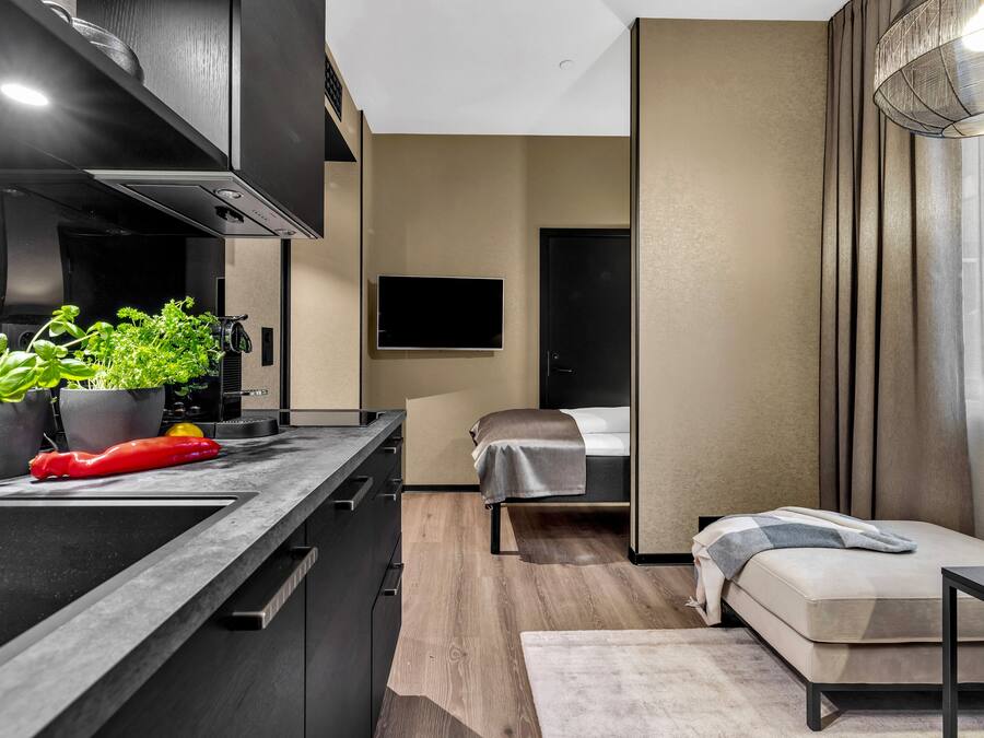 A modern kitchen with a built-in stove, a dining area with a table and chairs, a bed with a bedside table, and a large window with curtains.