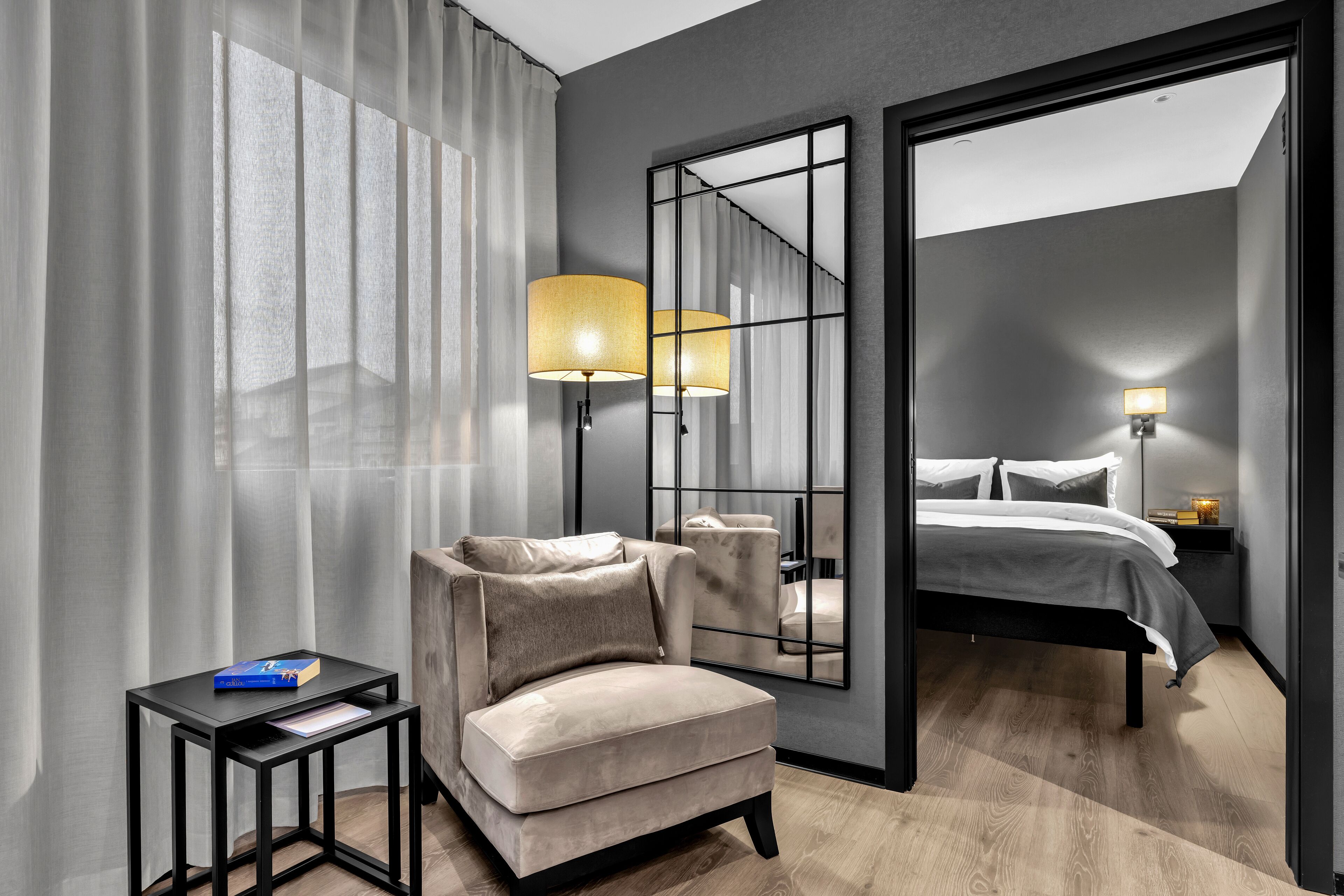 Una habitación de hotel moderna con sofá, una mesita, cama y un espejo grande.