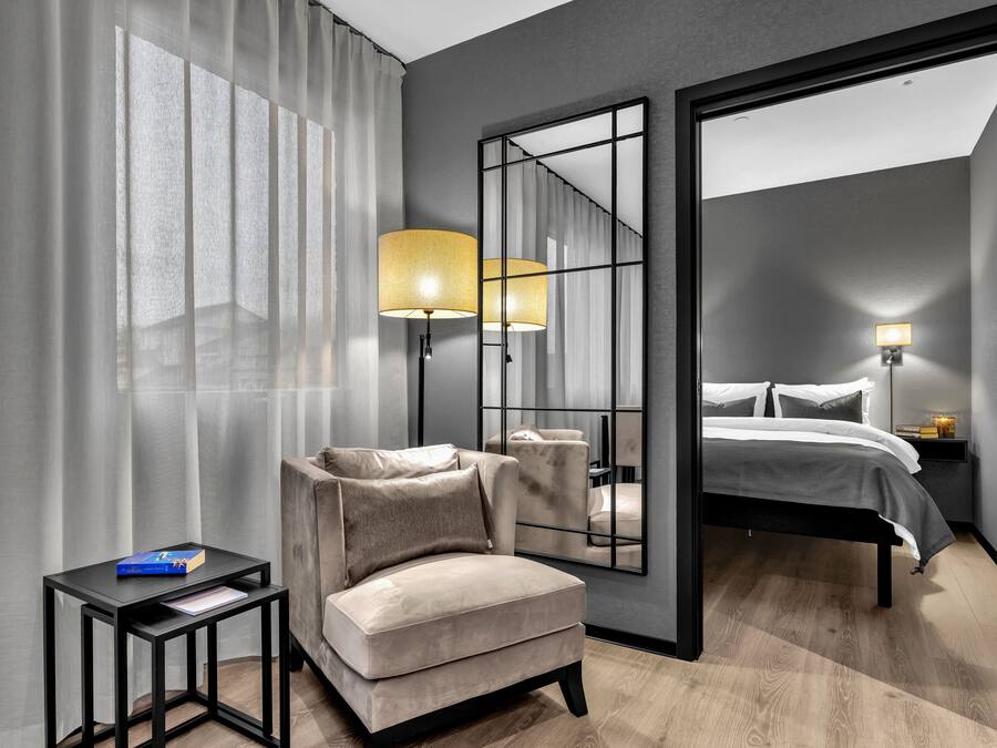 Una habitación de hotel moderna con sofá, una mesita, cama y un espejo grande.