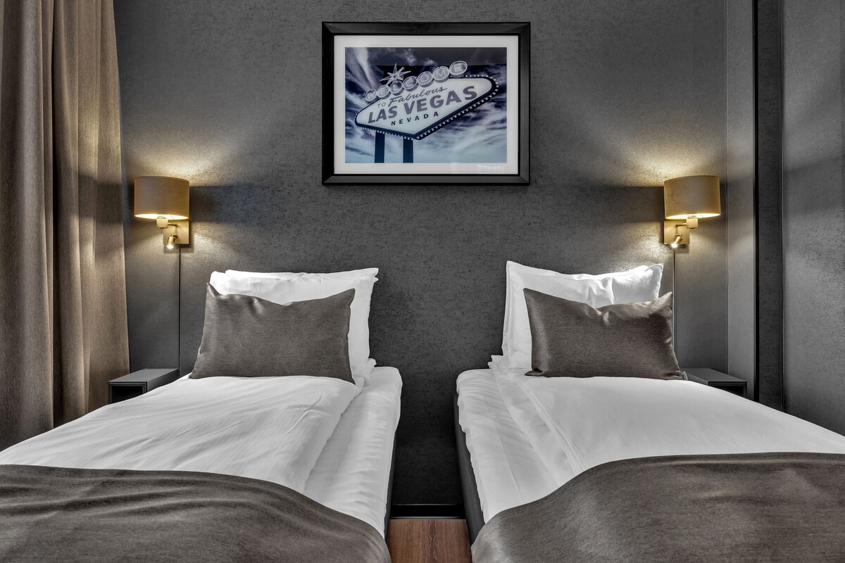Une chambre d’hôtel avec deux lits, un tableau encadré représentant l’enseigne de Las Vegas et des lampes fixées au mur.
