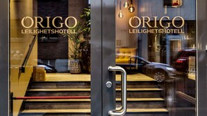 Entrada de un hotel con puertas de vidrio, una escalera y un automóvil estacionado afuera.