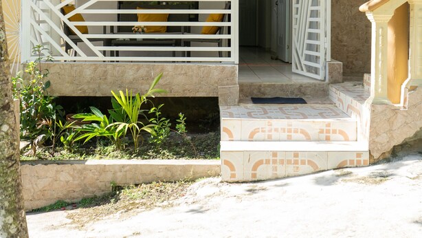A building with a beige facade, white railings, and a small garden area with plants. - Cozy house with 3 bedrooms, a 10-minute walk to the Samana boardwalk. (Samaná)