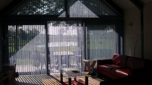 A room with a large sliding glass door, a red leather sofa, a glass coffee table, and a TV on a wooden stand. - Ottenskamp4 en Het Achterhuis (Siebengewald)