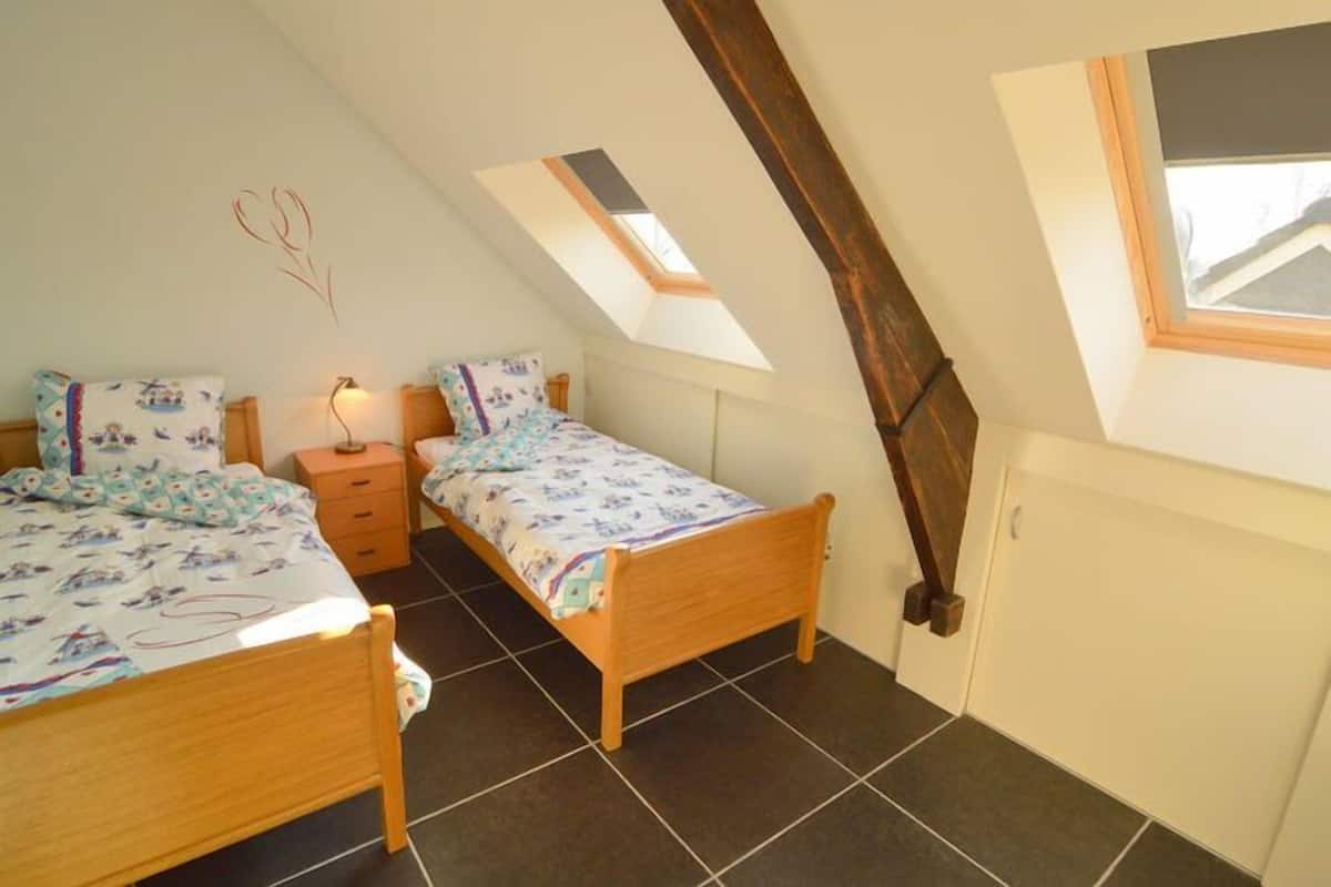 Une chambre avec deux lits, une table de chevet, une lampe fixée au mur et un puits de lumière.