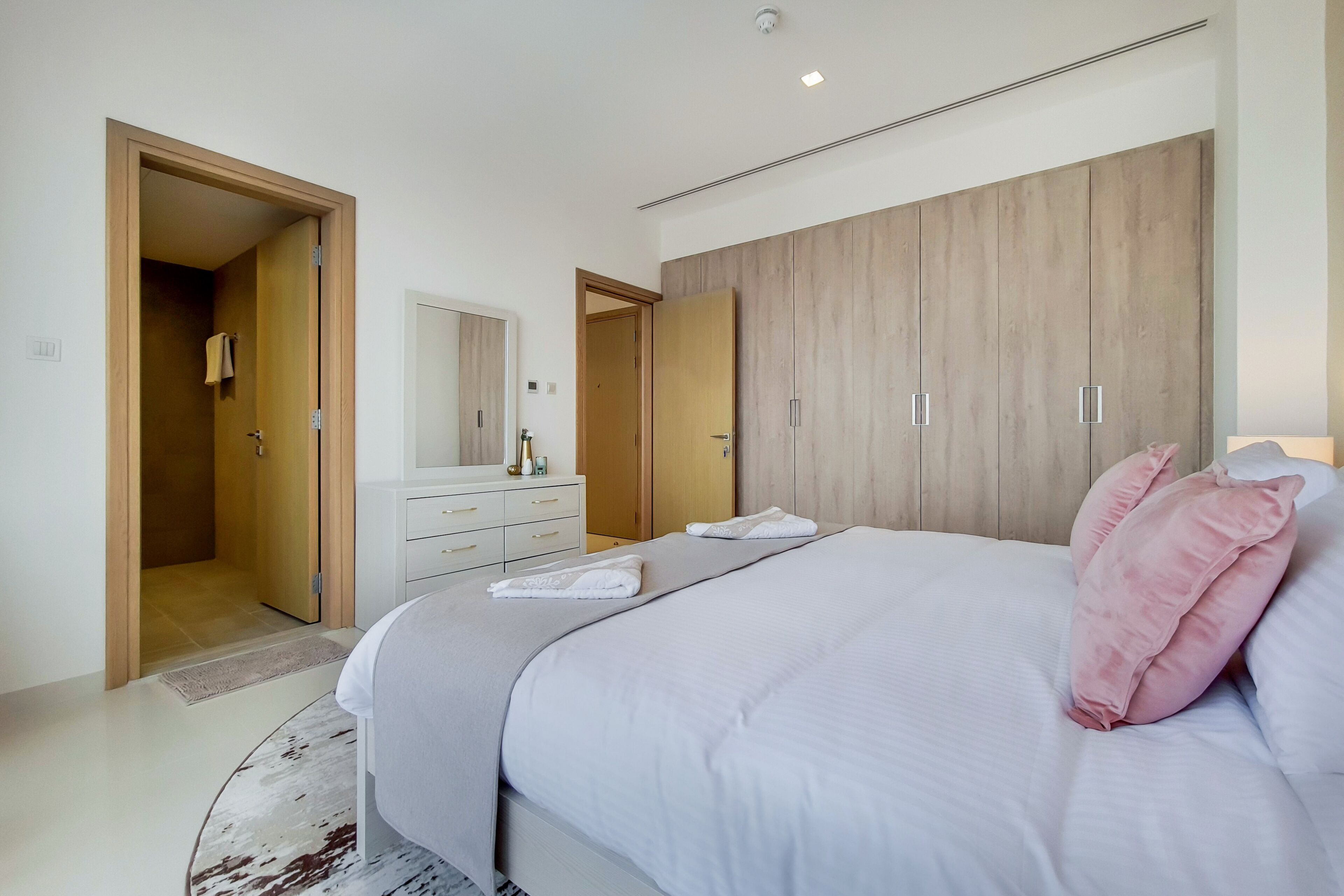 A modern bedroom with a large bed, wooden wardrobe, and a white dresser.