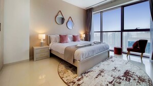 A modern hotel room with a large bed, bedside lamps, a round rug, and a view of the city through large windows.