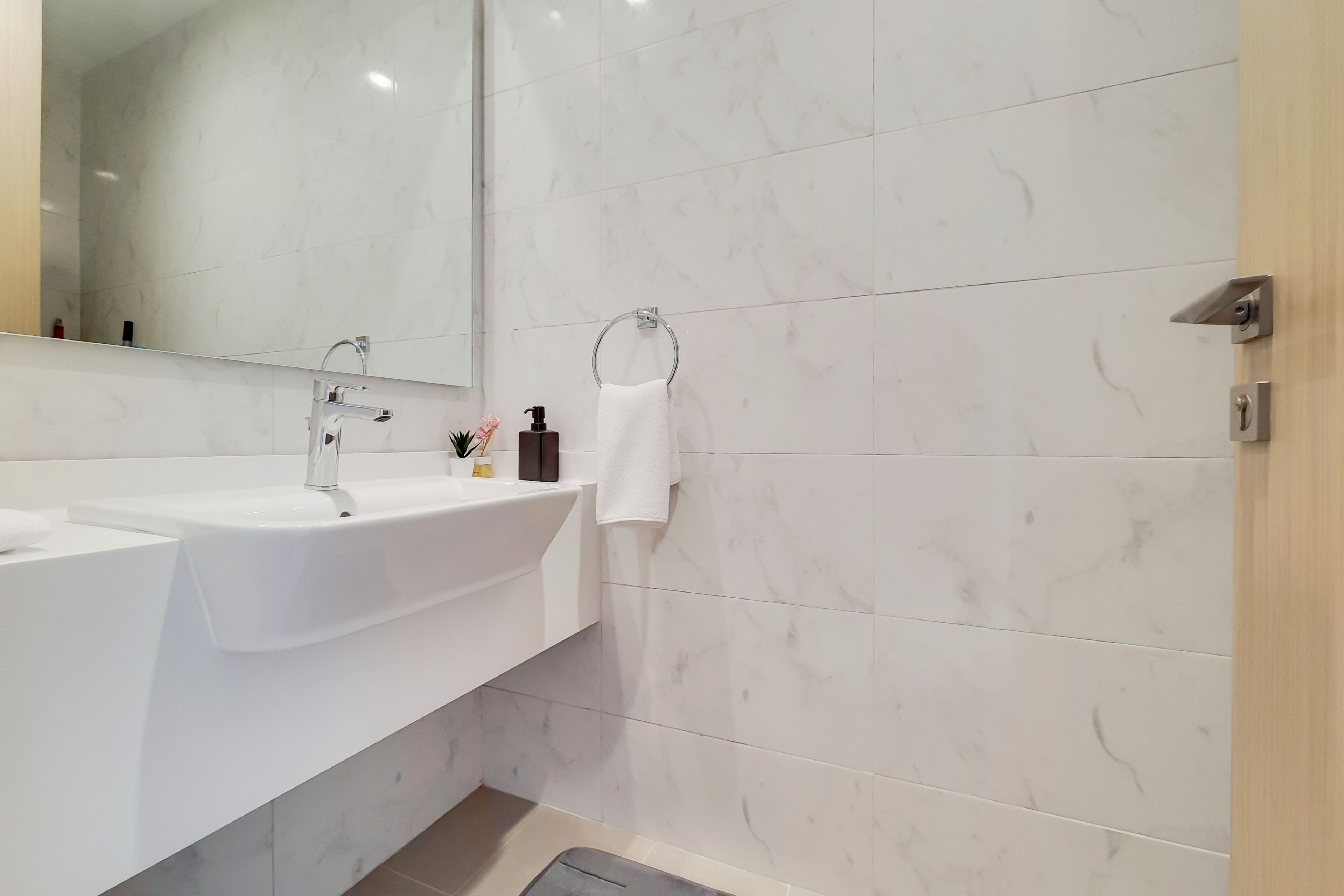 A modern bathroom with a white sink, a large mirror, and a towel ring.