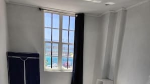 Une chambre avec un lit, une armoire, une fenêtre donnant sur la mer et une étagère blanche.