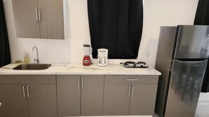 Une cuisine moderne avec des meubles gris, un réfrigérateur en acier inoxydable, un évier, un mixeur rouge et une machine à café.