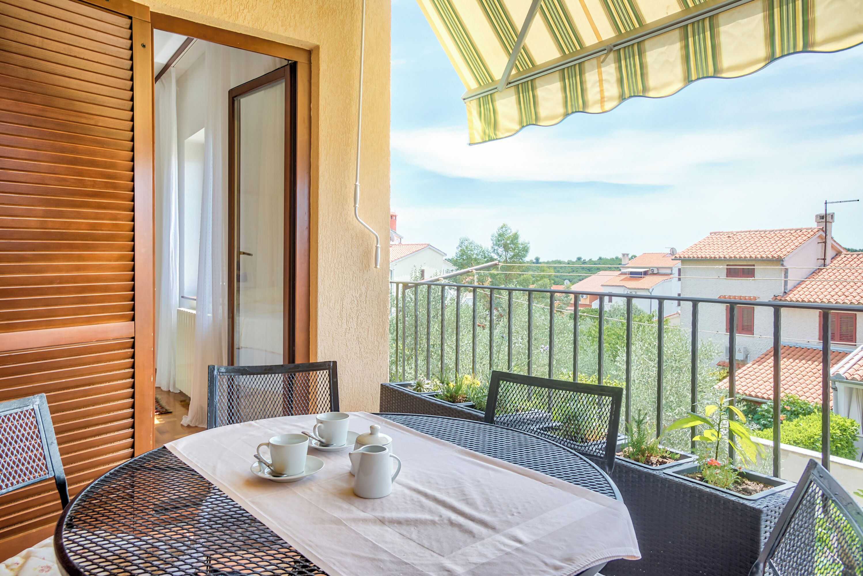 A balcony with a table set for tea, chairs, and potted plants.