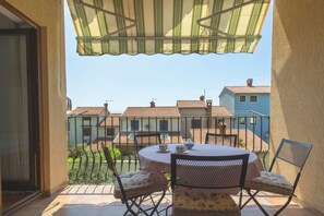 A balcony with a table and chairs, a view of neighboring houses, and a green awning.