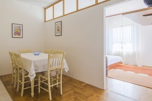 A room with a wooden dining table, chairs, and a bed with a pink rug.