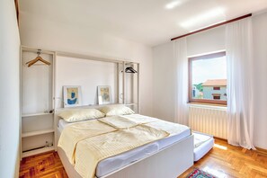 A bedroom with a bed, a window with curtains, a radiator, and a wooden floor.
