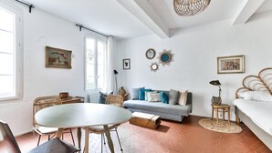 Une pièce comprenant une table de salle à manger ronde, un canapé avec des coussins, un lit et un luminaire suspendu.