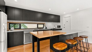 Cocina moderna con armarios oscuros, una isla de madera y taburetes de bar.