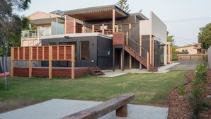 Una moderna casa a due piani con una zona esterna coperta, un terrazza in legno e una scala che conduce al piano superiore.