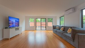 Un salón amplio con televisor de pantalla plana, un sofá gris y ventanas grandes que ofrecen vistas al exterior.
