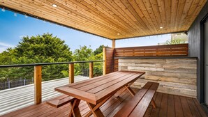Un patio in legno con tavolo e panche, un muro in pietra e vista sugli alberi.