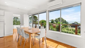 A modern kitchen with a wooden dining table and white chairs, large windows with a view of greenery and a body of water. - Sea to Sunset View in Ventnor (Ventnor)