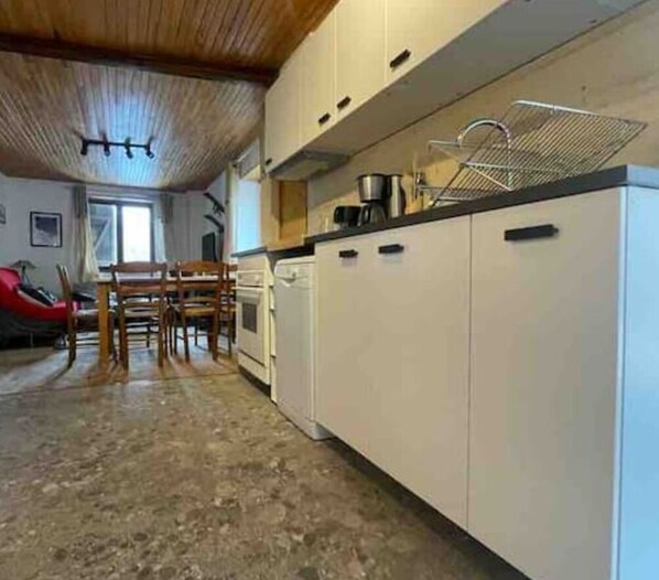 A kitchen with white cabinets, a wooden ceiling, and a dining area with chairs and a table.