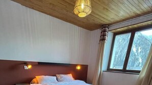Quarto com cama, piso de madeira, uma janela grande e luminária no teto.