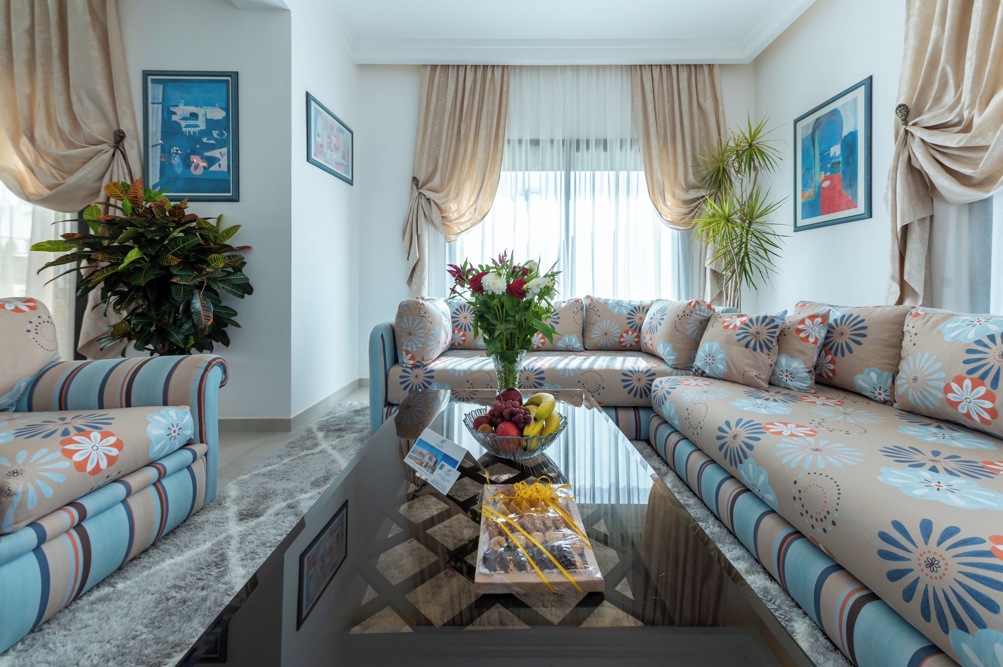 A living room with a sofa set, a coffee table with fruit and a gift, and a large plant.