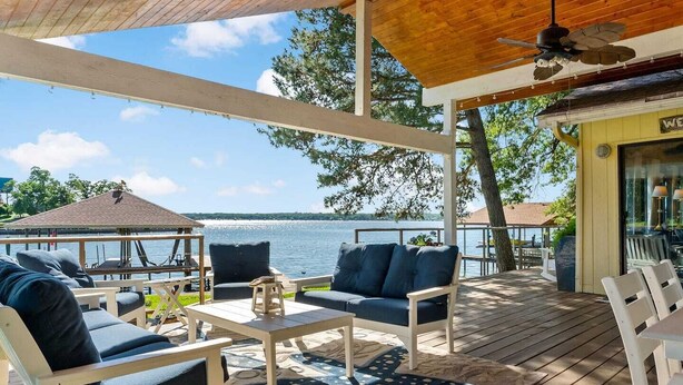 A covered outdoor seating area with a view of the water, wooden furniture, and a small table.