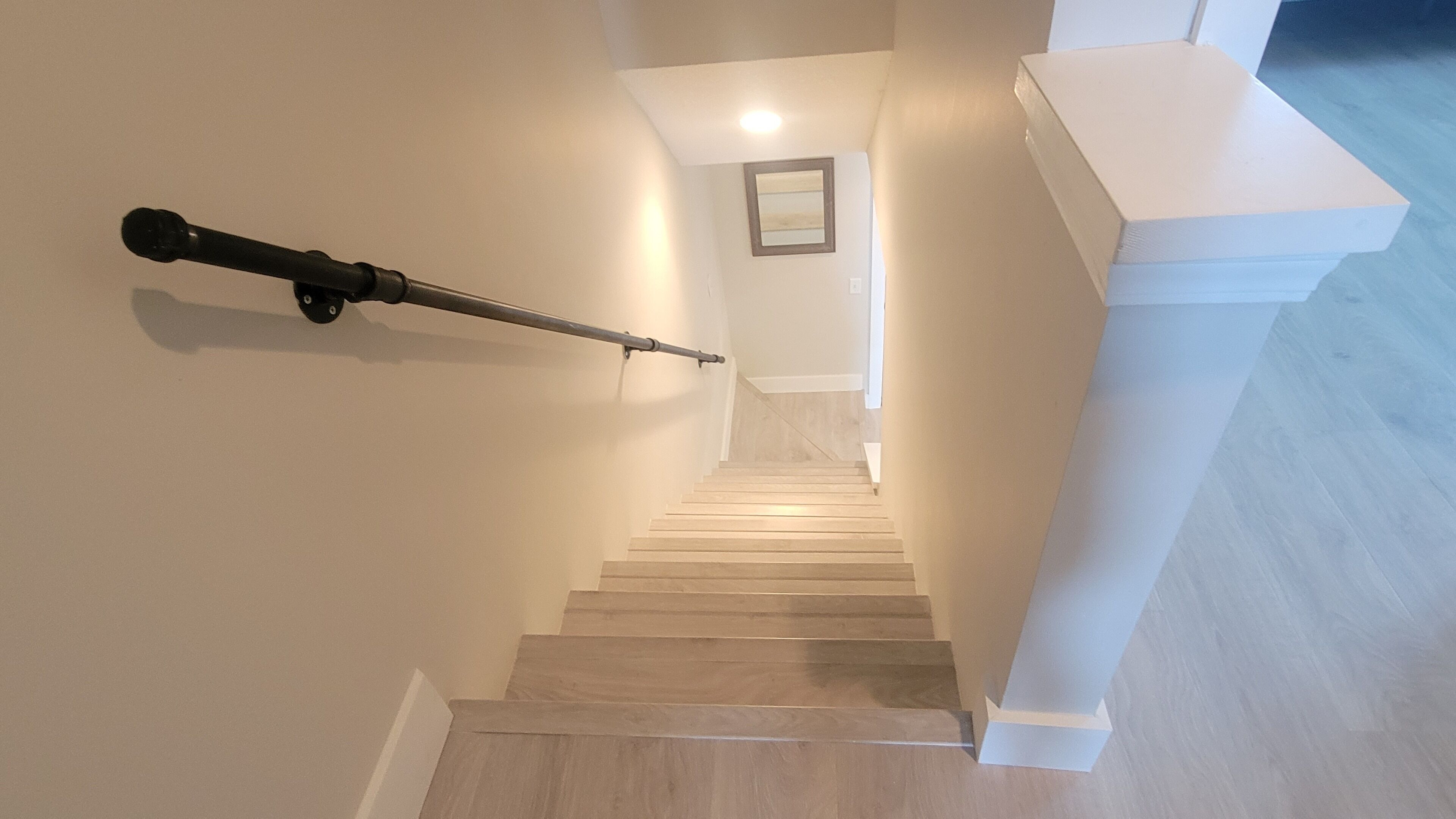 A staircase with a handrail, white walls, and a framed picture on the wall.