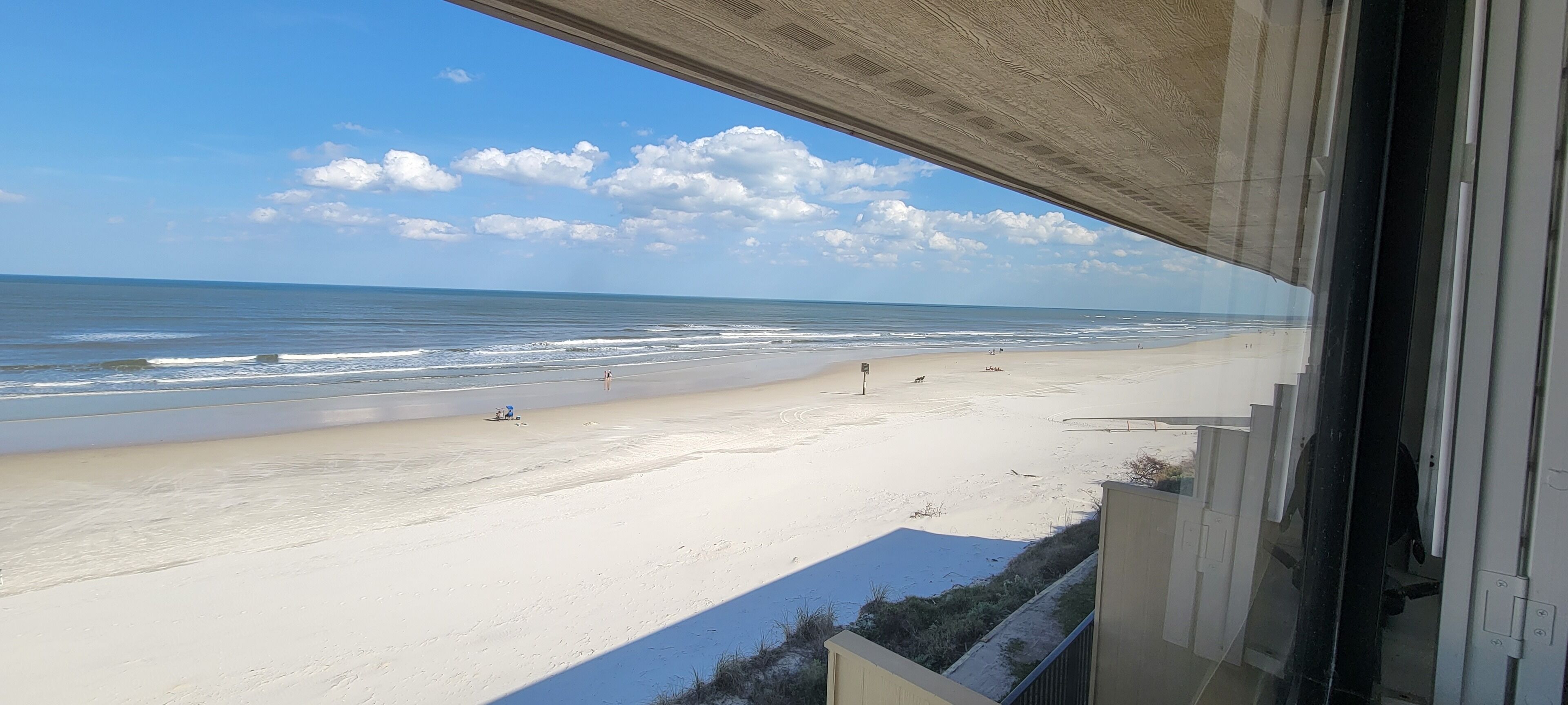 A beach view from a balcony with a clear sky and calm sea.