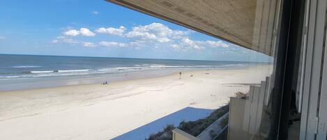 A beach view from a balcony with a clear sky and calm sea.