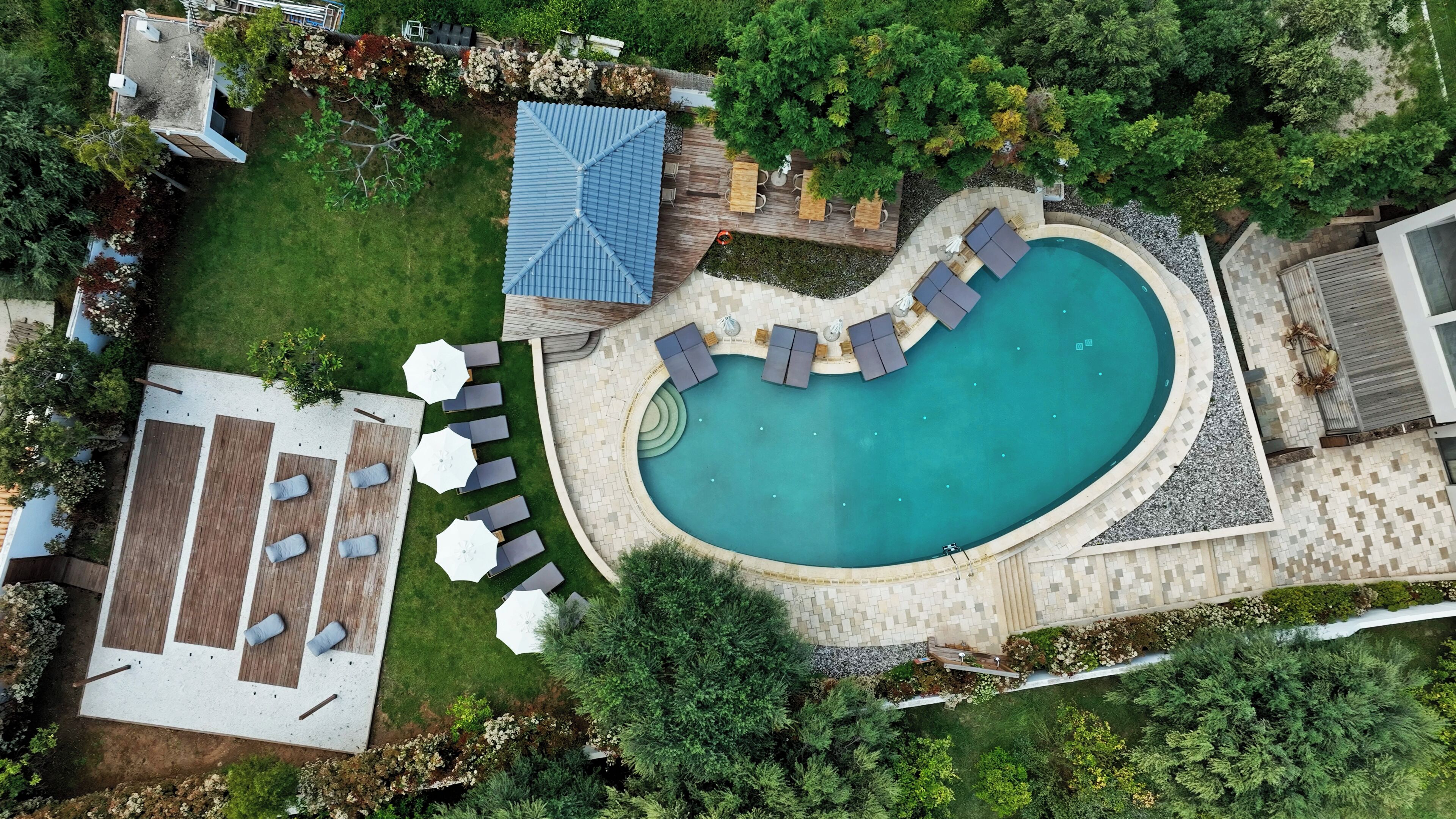 Vue aérienne d’une cour arrière avec une piscine, des chaises longues, un espace barbecue et une terrasse couverte.