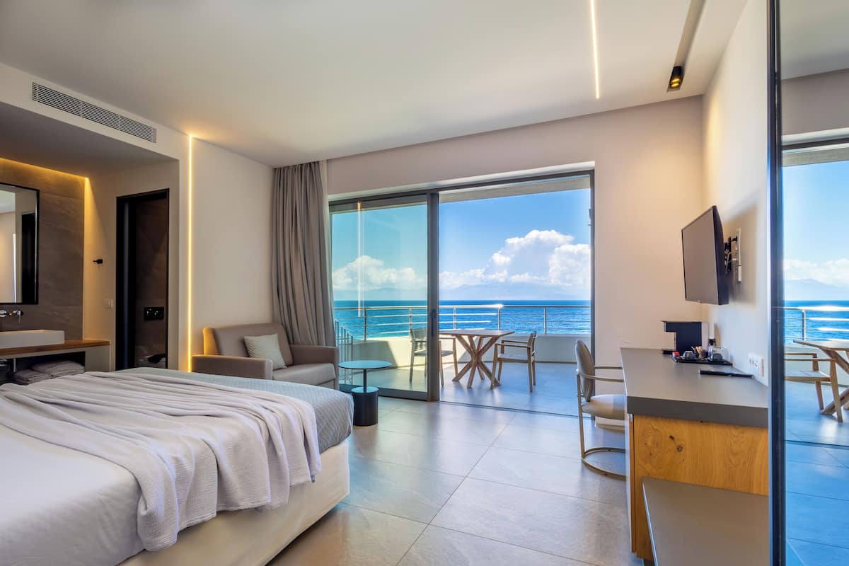 Ein modernes Hotelzimmer mit einem großen Bett, einem Schreibtisch und einem Balkon mit Meerblick.