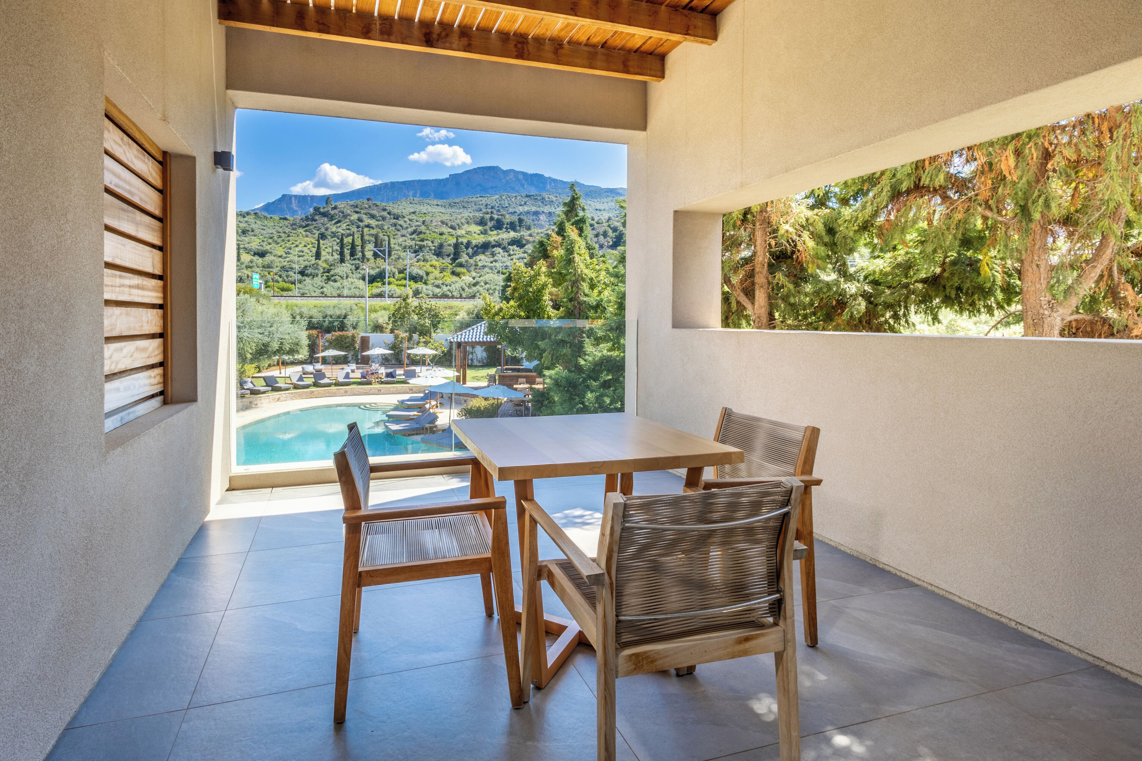 A patio with a table and chairs, a view of a swimming pool and mountains.