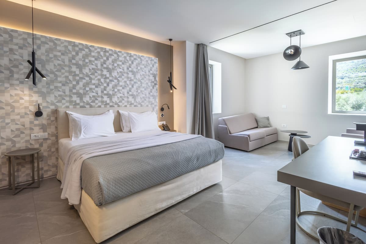 Ein modernes Schlafzimmer mit einem großen Bett, Nachttischen, einer Couch, einem Esstisch und Blick auf Grün.