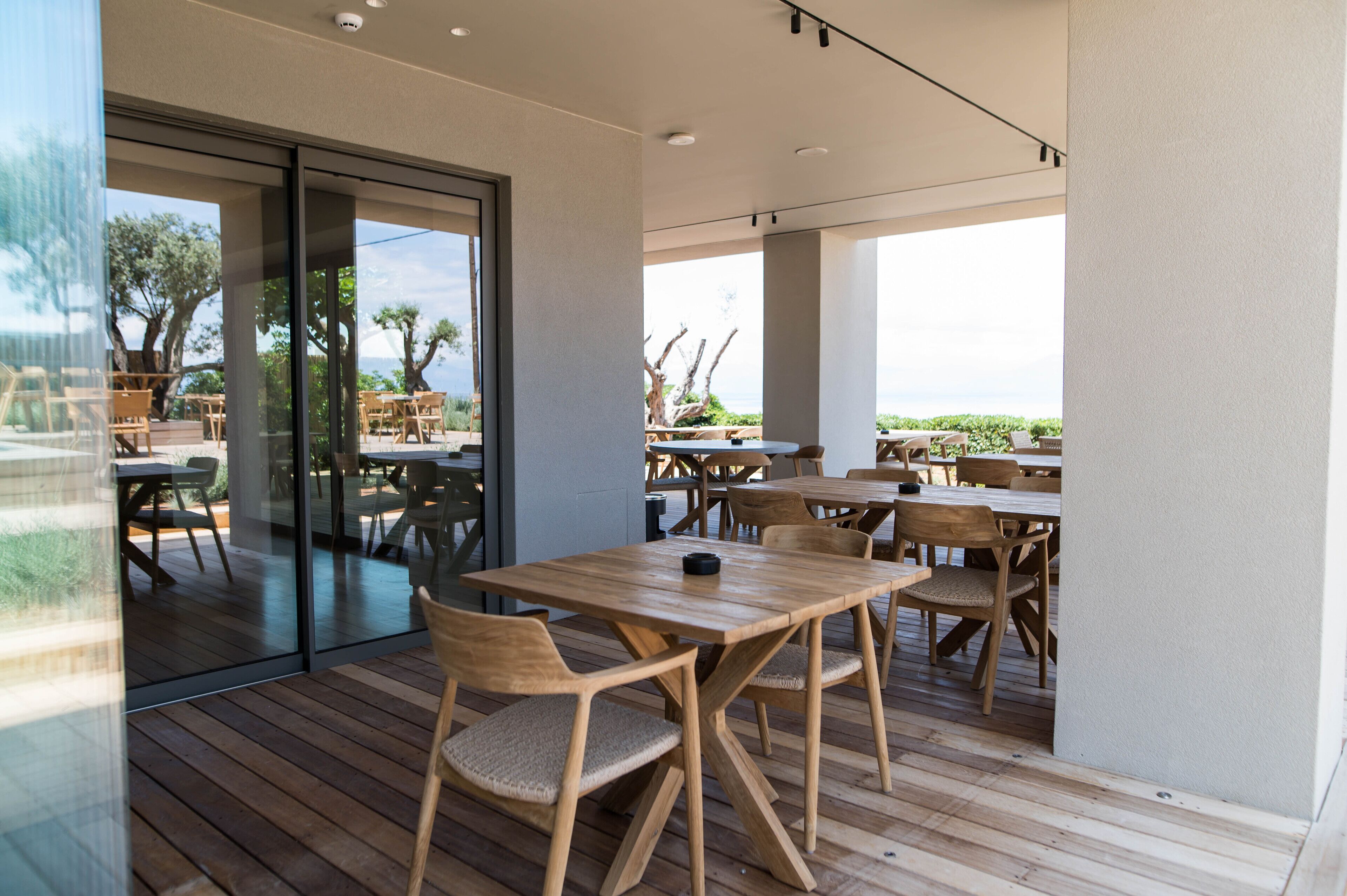 Un espace de restauration en plein air avec des tables et des chaises en bois, de grandes fenêtres et une vue sur l’extérieur.