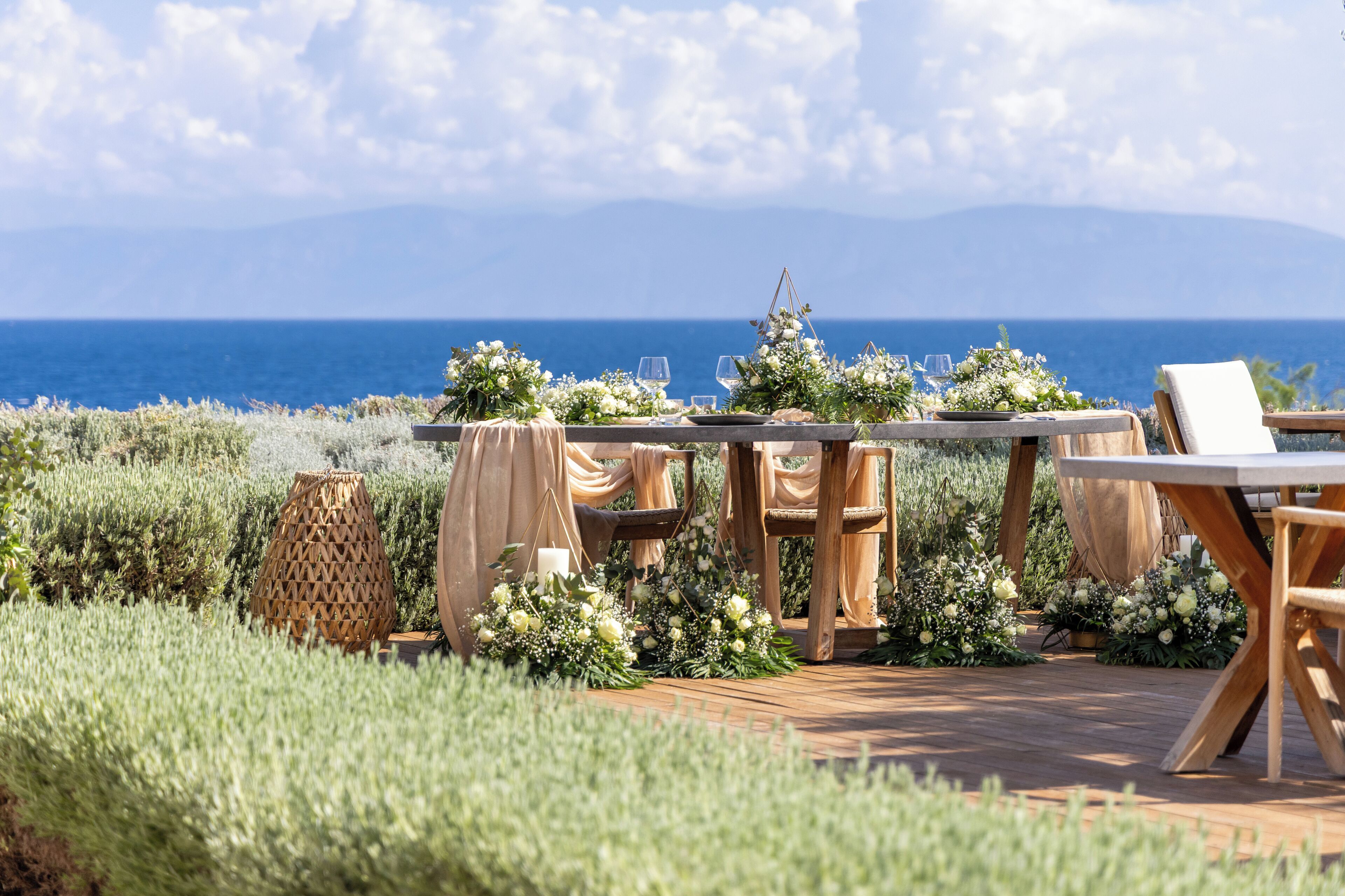Un espacio de comedor al aire libre con vistas al mar, rodeado de vegetación y decorado con flores.