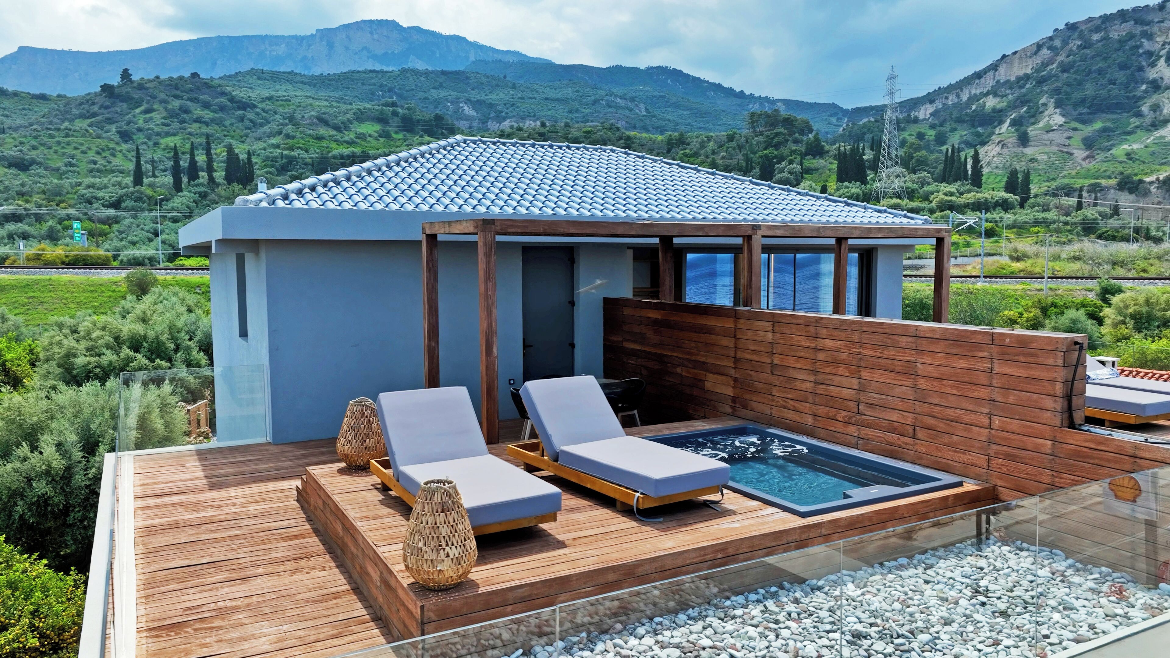 A modern outdoor pool area with lounge chairs and a hot tub, surrounded by wooden decking and pebbles.