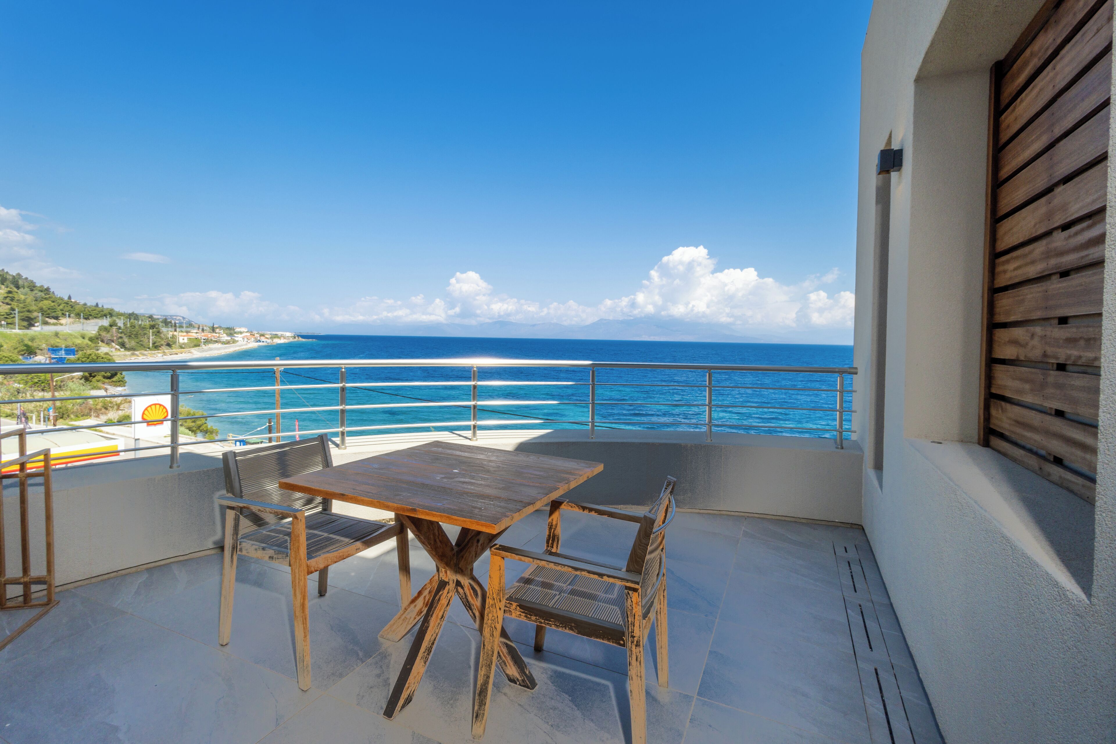 A balcony with a wooden table and chairs, overlooking a beach and ocean.